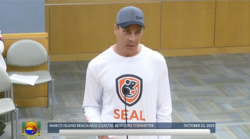 A speaker in a Seal Em Out shirt at a Marco Island public meeting